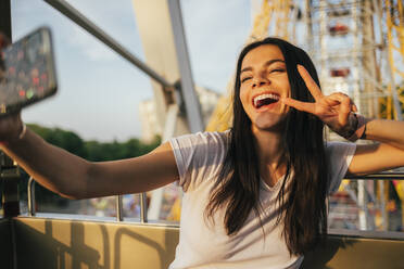 Fröhliche Frau auf dem Riesenrad, die ein Handy benutzt, während sie ein Selfie im Vergnügungspark macht - OYF00233