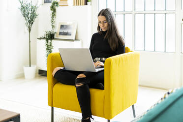 Young woman using laptop for blogging while sitting on chair at home - GIOF09430