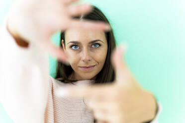 Schöne junge Frau macht Finger Rahmen gegen grüne Wand - GIOF09498