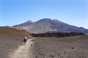 Senior man hiking along trail stretching across brown barren landscape of Tenerife island - WWF05556