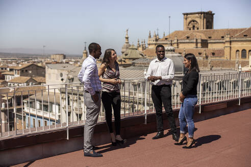 Smiling male and female entrepreneurs discussing on rooftop of office building during break - LJF01790