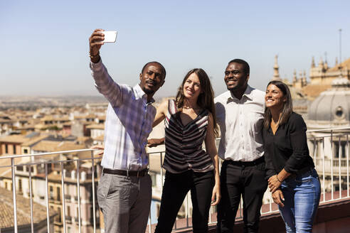 Happy multi-ethnic colleagues taking selfie at office rooftop during break - LJF01791