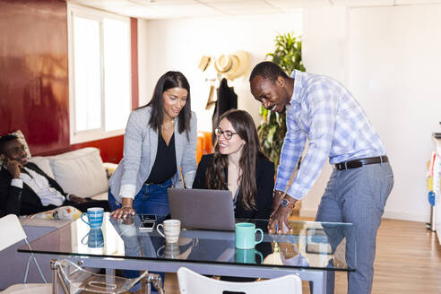 Smiling male and female colleagues discussing over laptop during meeting in coworking office - LJF01814