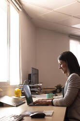 Lächelnde Unternehmerin mit Laptop am Schreibtisch im Büro - LJF01820