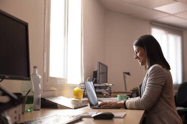 Lächelnde Geschäftsfrau mit Laptop in einem Coworking-Büro - LJF01821