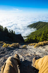 Mann sitzt auf einem Berg vor einer Wolkenlandschaft im Nationalpark El Teide, Teneriffa, Spanien - SIPF02211