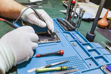 Technician examining damaged mobile phone at workbench at repair shop - LJF01840