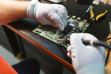 Technician soldering circuit board of electrical component at workbench in electronics repair shop - LJF01847