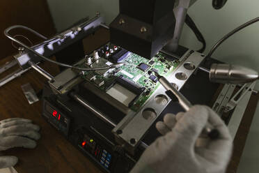 Electronics expert examining damaged circuit board at repair shop - LJF01849
