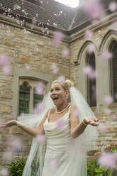 Überrascht junge Braut stehend inmitten von Blütenkonfetti in der Kirche - AJOF00467