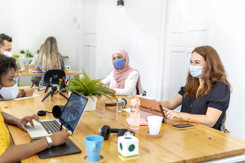 Employees wearing face mask sitting at social distance while working at office - MPPF01182