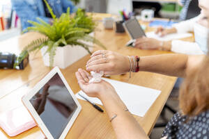 Mid adult woman using hand sanitizer while working with coworker at office - MPPF01187