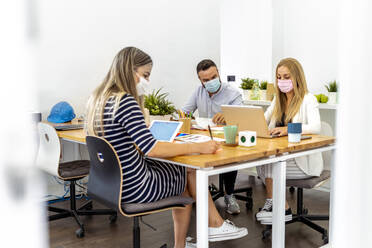 Geschäftsleute tragen Gesichtsmaske beim Sitzen am Schreibtisch im Büro - MPPF01194