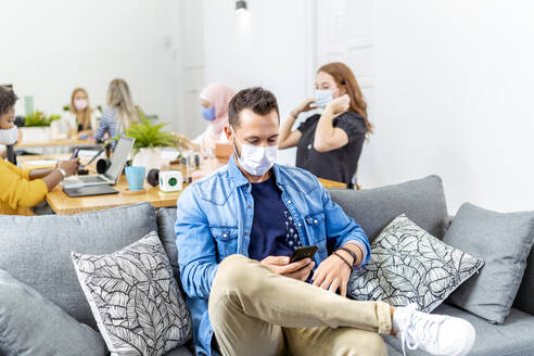 Mid adult man using mobile phone while sitting with coworker in background at office - MPPF01198