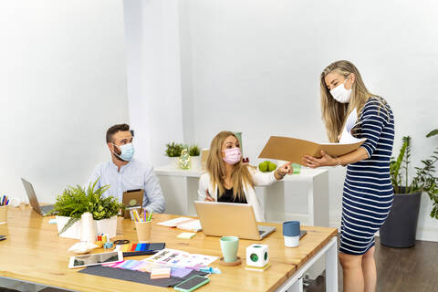 Employee wearing face mask discussing file while working with coworker at office stock photo