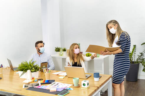 Employee wearing face mask discussing file while working with coworker at office - MPPF01201