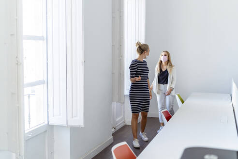 Mid adult women wearing face mask talking while walking at office - MPPF01209