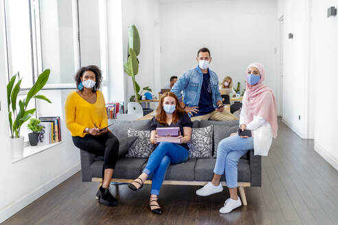 Employees wearing face mask maintaining social distance while sitting with coworker in background at office during COVID-19 - MPPF01211