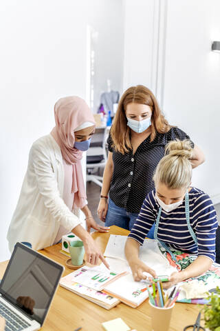 Coworker wearing face mask having discussion while using mobile phone at office stock photo