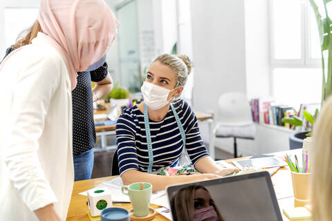 Coworker wearing face mask discussing while using mobile phone at office stock photo
