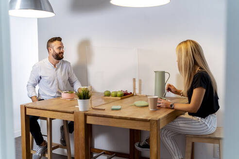 Man and woman talking while having food and drink at table in office - MPPF01225