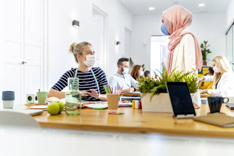 Female coworker having discussion while working with employees in background at office stock photo