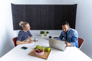 Female and male coworker discussing while working on laptop at office - MPPF01234