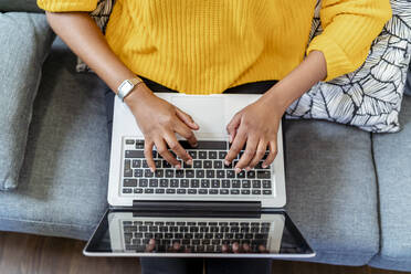 Junge Frau benutzt einen Laptop, während sie auf dem Sofa im Büro sitzt - MPPF01242