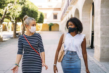 Women wearing face mask talking while walking in city - MPPF01249