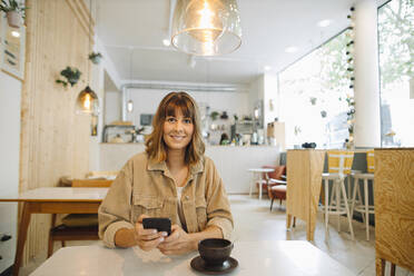 Businesswoman using smart phone while sitting in cafe - GUSF04551