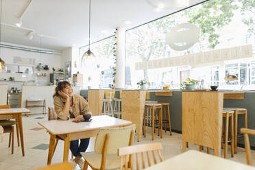 Young female entrepreneur laughing with hand on chin sitting in cafe - GUSF04555