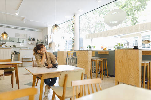 Junge Unternehmerin, die mit der Hand am Kinn in einem Café sitzt und nach oben schaut - GUSF04556