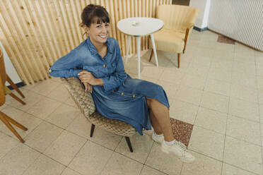 Lächelnde Unternehmerin sitzt auf einem Stuhl in einem Cafe - GUSF04562