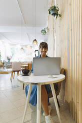 Unternehmerin mit Laptop in einem Café sitzend - GUSF04564