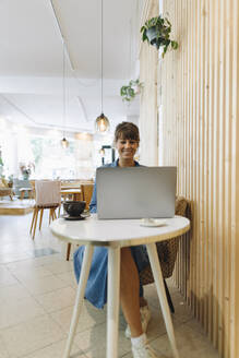 Unternehmerin mit Laptop in einem Café sitzend - GUSF04564