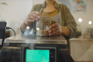 Mittelteil einer Besitzerin, die in einem Café Getreidegläser auf einer Waage wiegt - GUSF04575