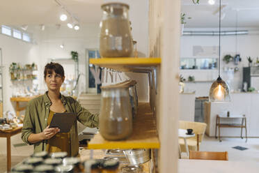 Geschäftsfrau, die ein digitales Tablet hält und wegschaut, während sie in einem Café vor Gläsern steht - GUSF04580