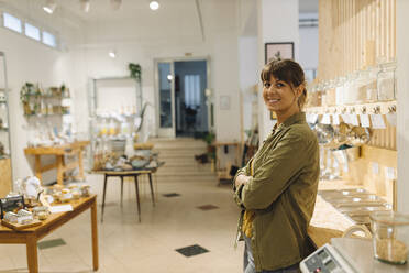 Smiling female owner with arms crossed standing in cafe - GUSF04583