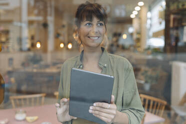 Geschäftsfrau, die einen digitalen Tisch benutzt und durch ein Fenster schaut, während sie in einem Café steht - GUSF04588