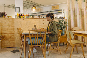 Weiblicher Besitzer arbeitet am Laptop, während er in einem Café sitzt - GUSF04591
