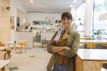 Female owner with arms crossed napkin on shoulder standing in coffee shop - GUSF04593