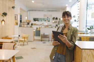 Lächelnde Besitzerin mit digitalem Tablet in einem Café stehend - GUSF04594