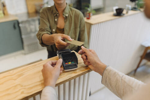 Mittelteil einer Unternehmerin, die einem Kunden an der Kasse eines Cafés eine Kreditkarte gibt - GUSF04603