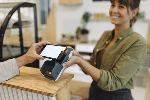 Ausgeschnittene Hand eines Kunden, der mit seinem Smartphone kontaktlos an der Kasse eines Cafés bezahlt, lizenzfreies Stockfoto