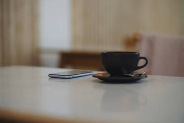 Smart phone and coffee cup on table in cafe - GUSF04610