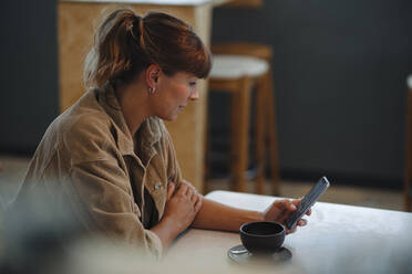 Weiblicher Besitzer Textnachrichten auf Smartphone sitzend im Café - GUSF04615