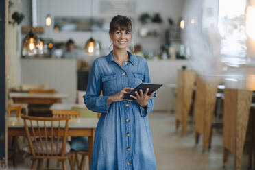 Lächelnde Unternehmerin, die ein digitales Tablet benutzt, während sie in einem Café steht - GUSF04623