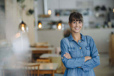 Smiling female owner with arms crossed standing in coffee shop - GUSF04627