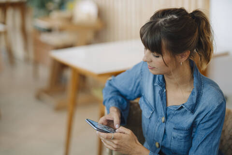 Young female owner text messaging on smart phone sitting in cafe stock photo