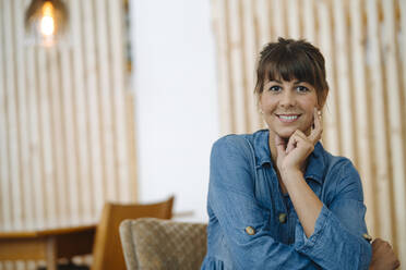 Smiling female owner with hand on chin sitting in cafe - GUSF04635